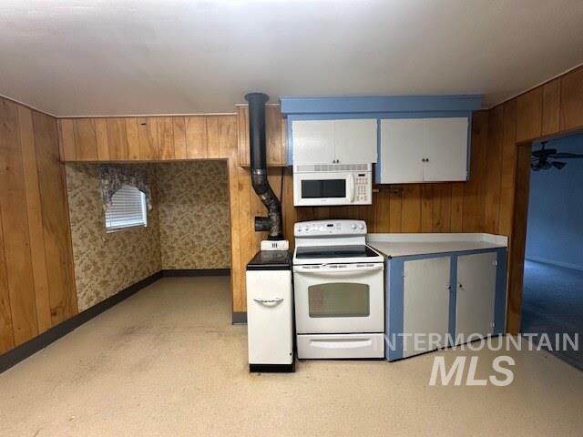 Kitchen with white appliances, white cabinets, light countertops, wooden walls, and light colored carpet