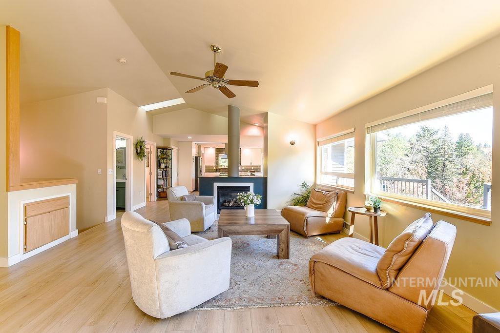 Living area featuring light wood-type flooring, lofted ceiling, a ceiling fan, and a fireplace