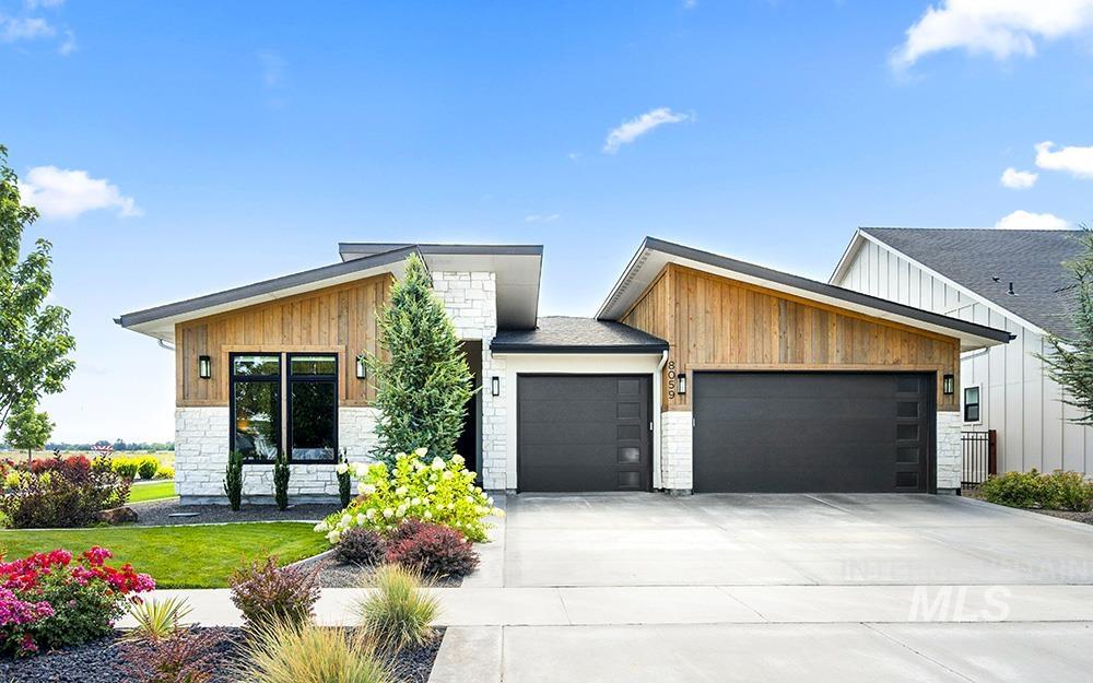 Contemporary house featuring a garage, stone siding, concrete driveway, board and batten siding, and a front lawn