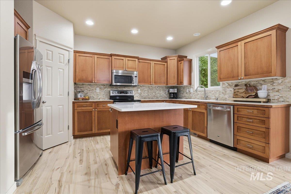 Kitchen with a breakfast bar, backsplash, stainless steel appliances, brown cabinetry, and recessed lighting