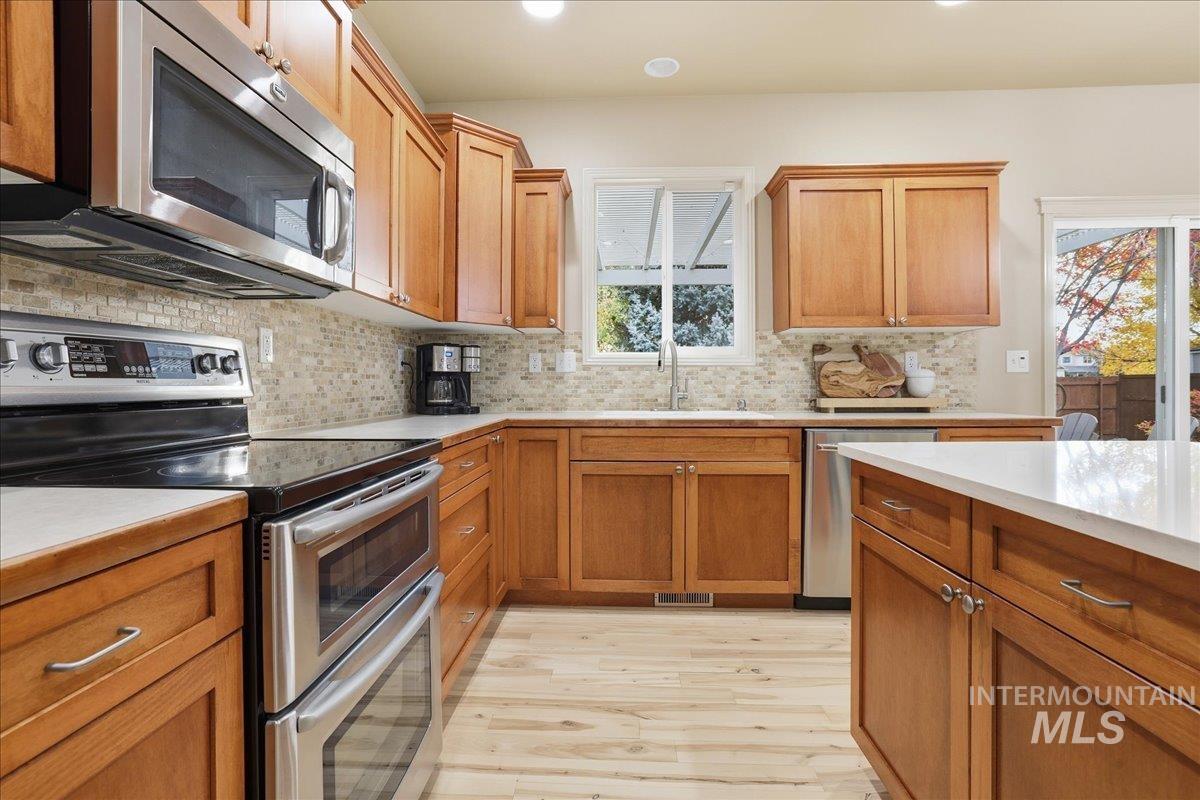 Kitchen featuring appliances with stainless steel finishes, tasteful backsplash, brown cabinets, light wood-type flooring, and recessed lighting