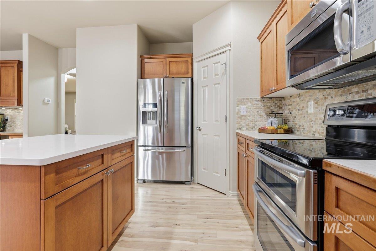 Kitchen featuring tasteful backsplash, stainless steel appliances, light countertops, brown cabinetry, and light wood finished floors