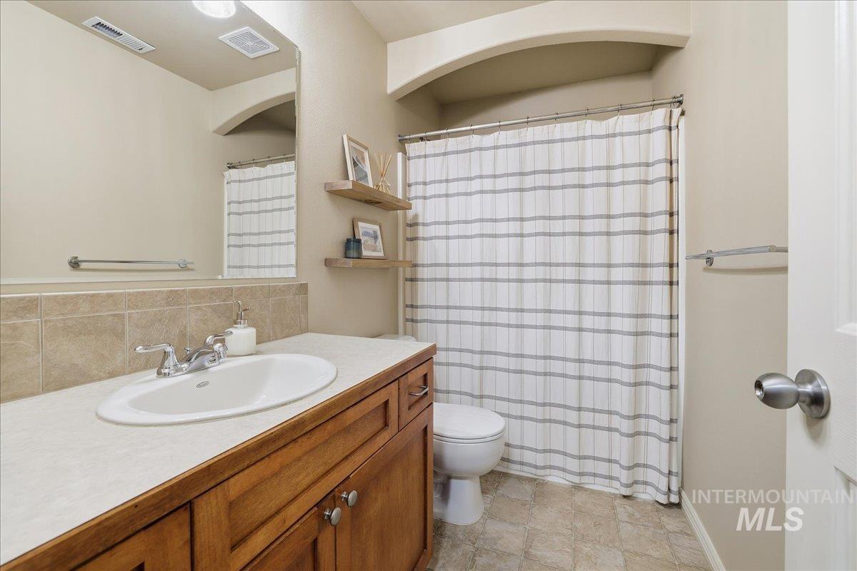 Bathroom with curtained shower, vanity, decorative backsplash, and light stone finish flooring