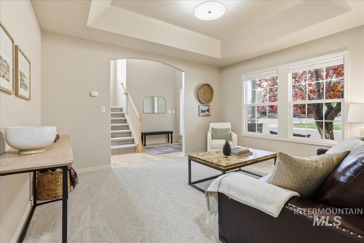 Living room featuring arched walkways, a raised ceiling, carpet flooring, stairs, and a textured ceiling