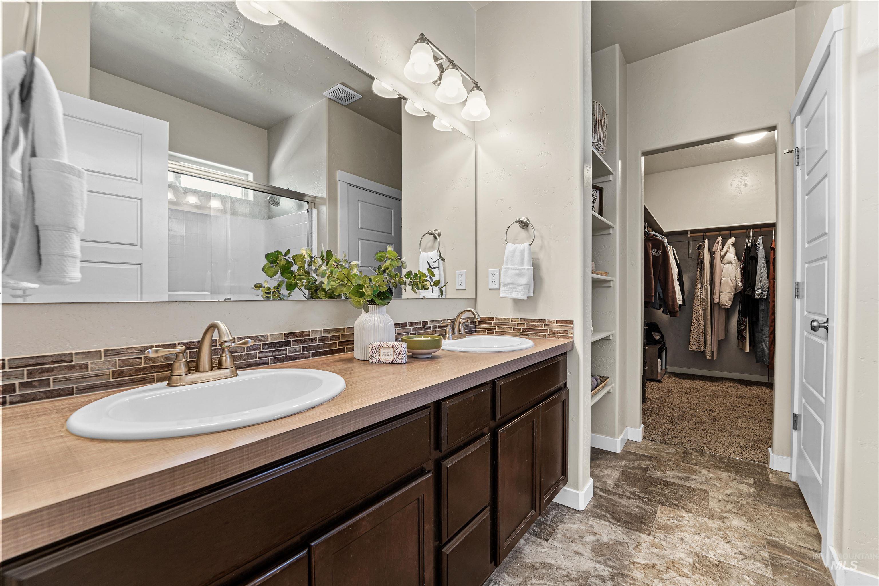 Bathroom featuring double vanity, a shower stall, stone finish floors, and a walk in closet