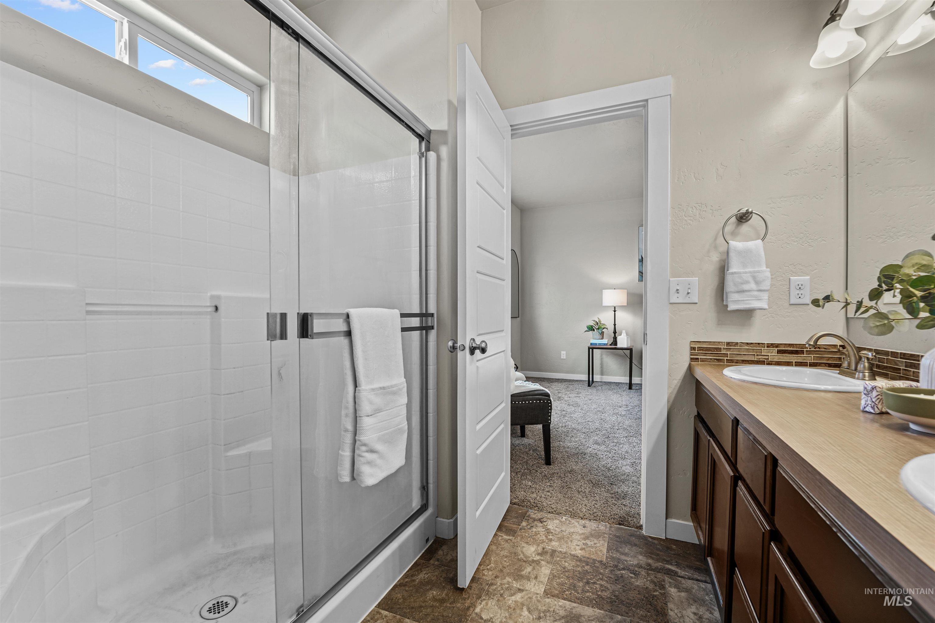 Ensuite bathroom featuring double vanity, dark stone finish floors, and a stall shower