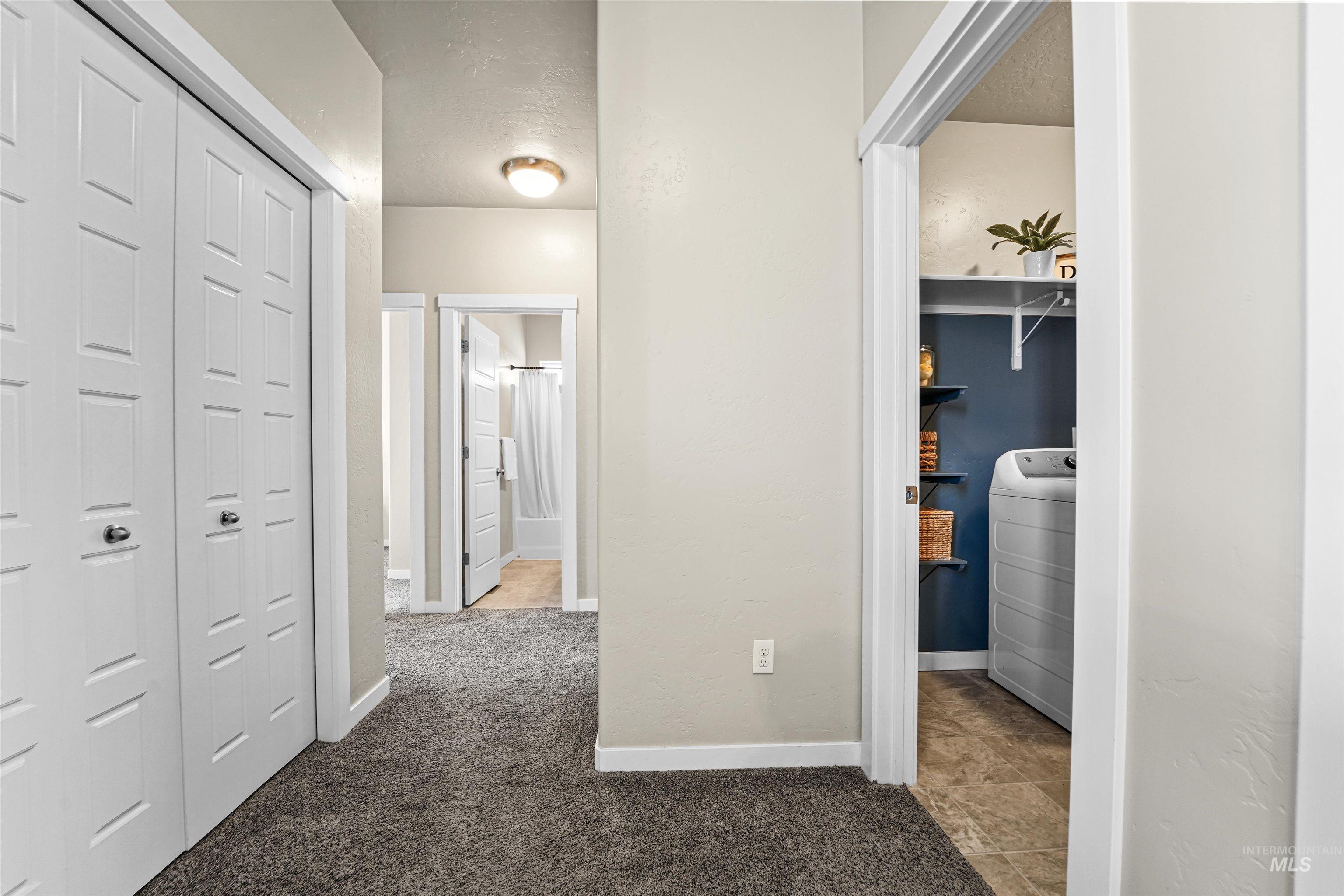 Corridor with washer / dryer, light colored carpet, and a textured ceiling