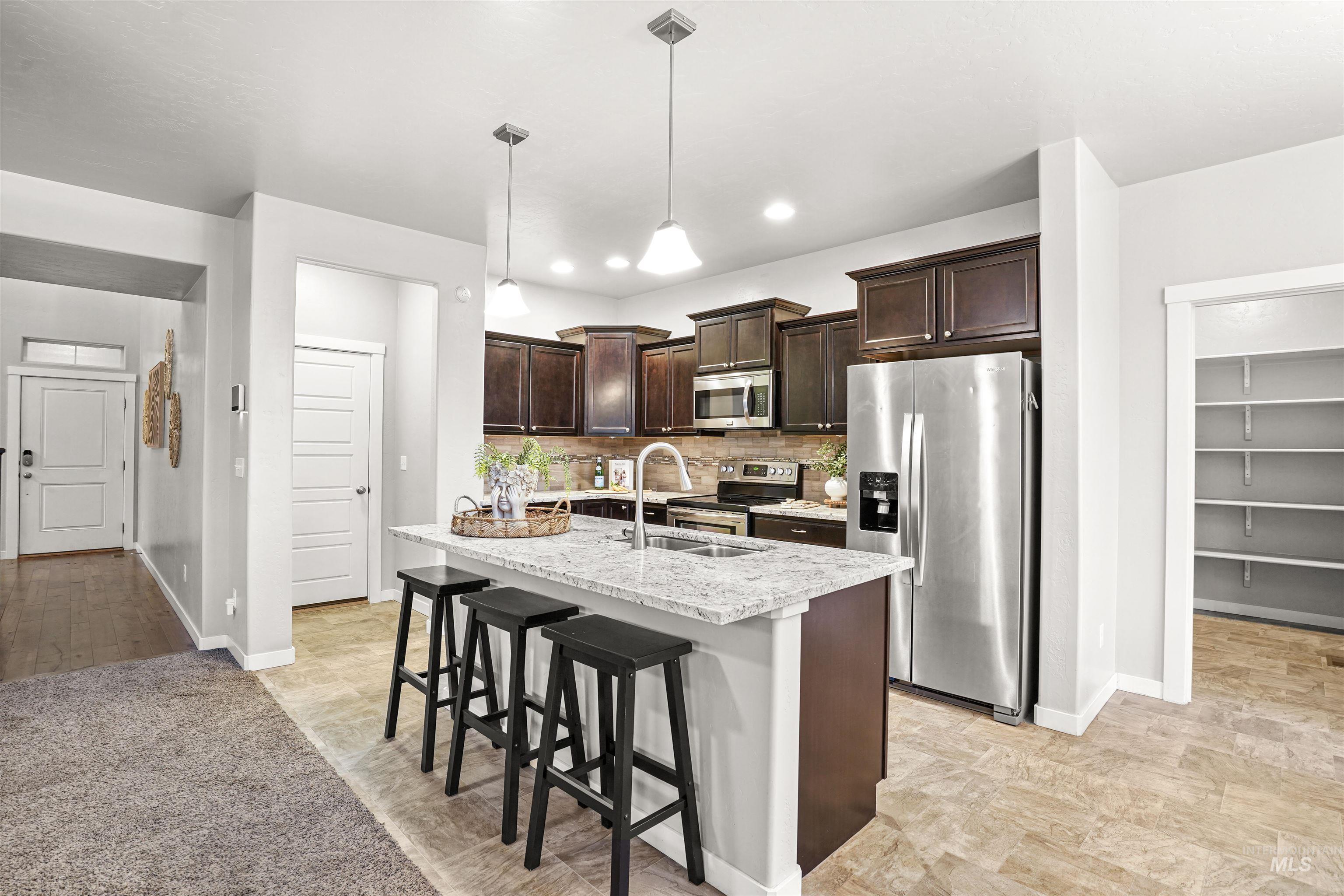 Kitchen with dark brown cabinetry, backsplash, appliances with stainless steel finishes, a breakfast bar, and pendant lighting