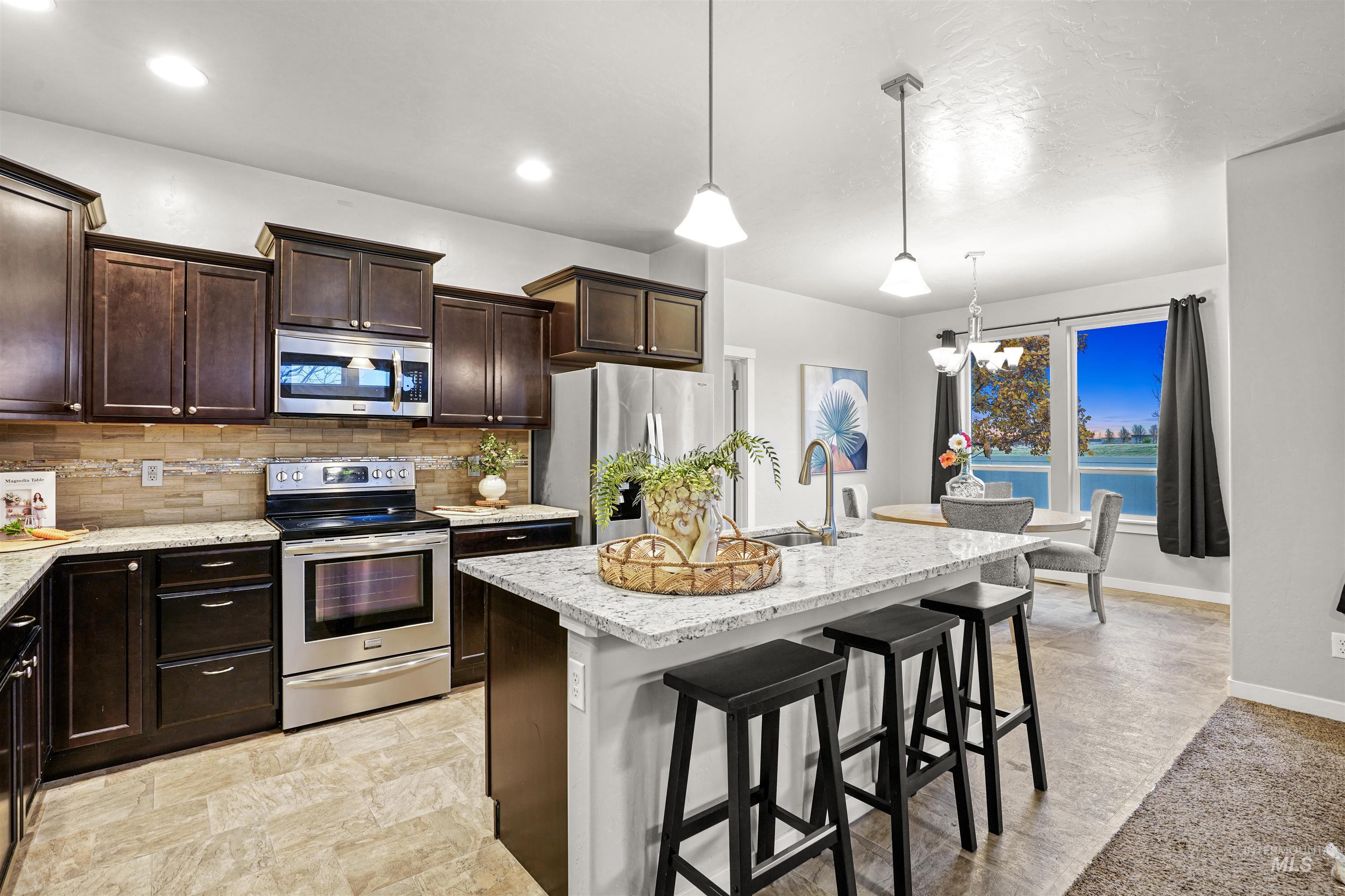 Kitchen with a breakfast bar area, appliances with stainless steel finishes, decorative backsplash, an island with sink, and dark brown cabinets
