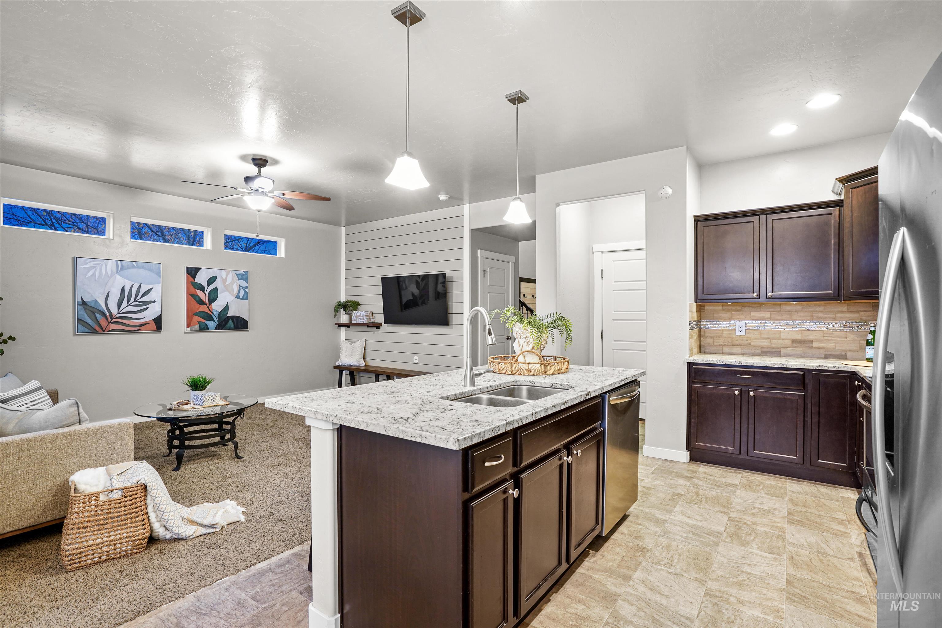 Kitchen featuring dark brown cabinets, light stone counters, a ceiling fan, and hanging light fixtures