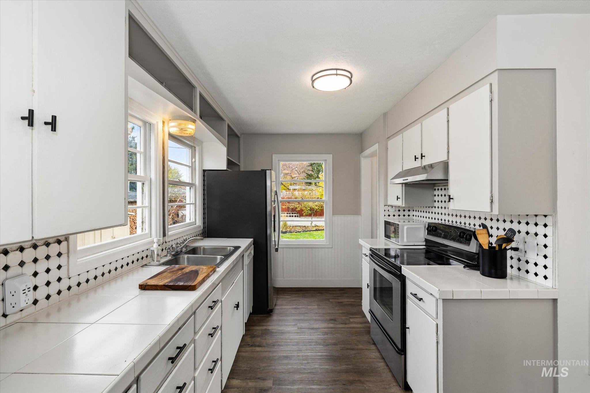 Kitchen featuring tile countertops, appliances with stainless steel finishes, white cabinetry, wainscoting, and decorative backsplash