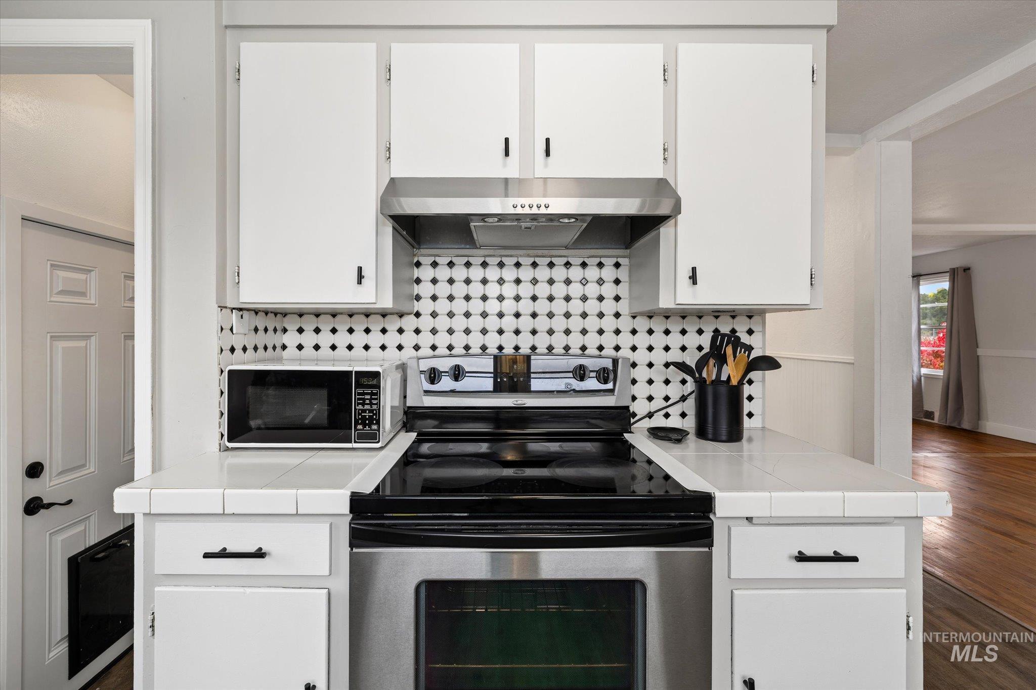 Kitchen featuring tile counters, stainless steel range with electric stovetop, backsplash, and dark wood-style flooring