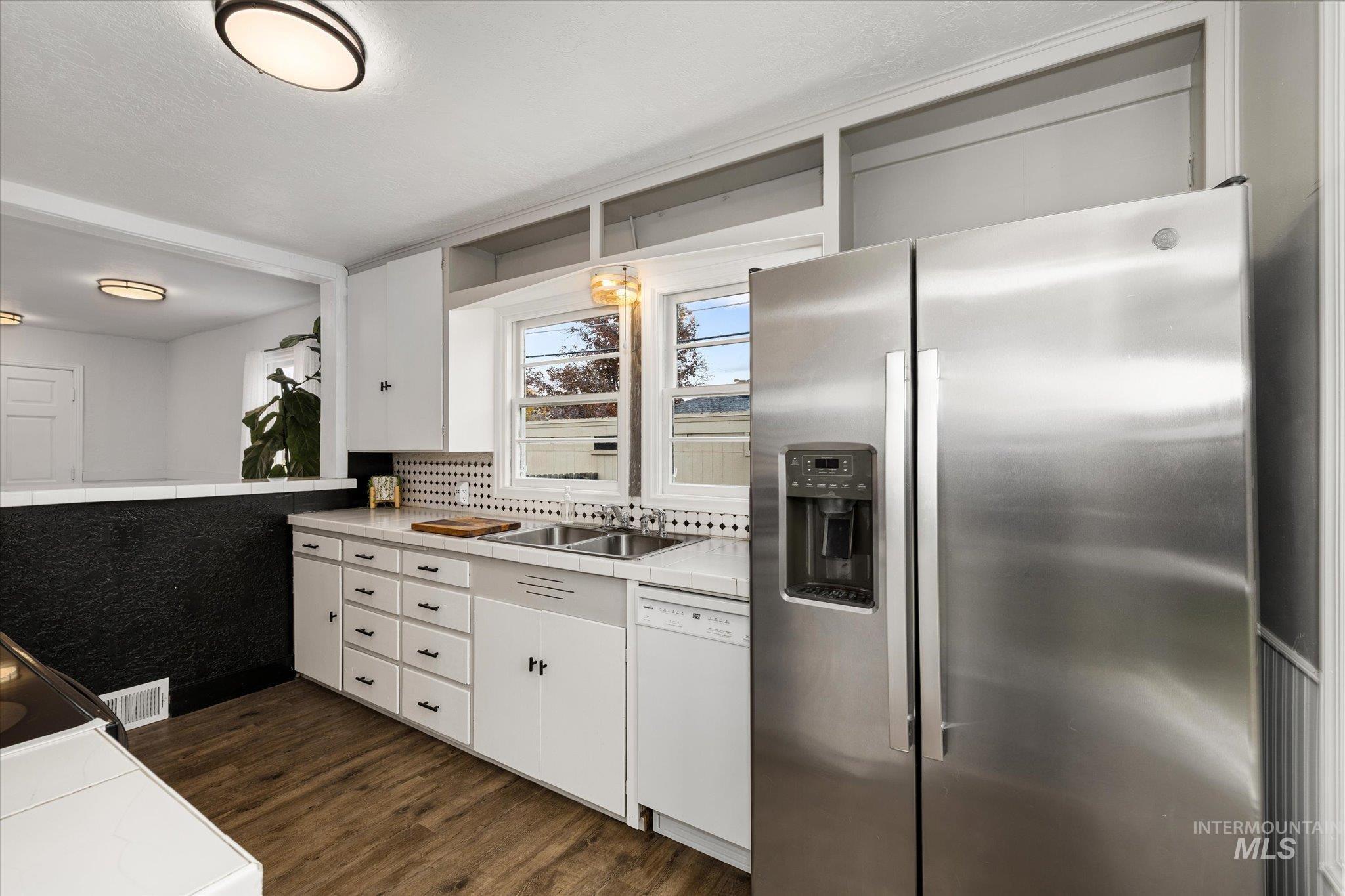 Kitchen featuring tile countertops, stainless steel fridge with ice dispenser, white cabinetry, dark wood-style flooring, and white dishwasher