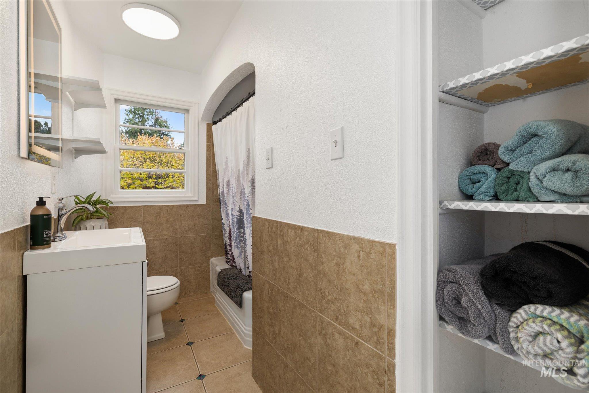 Bathroom with tile walls, a shower with curtain, tile patterned flooring, vanity, and a wainscoted wall