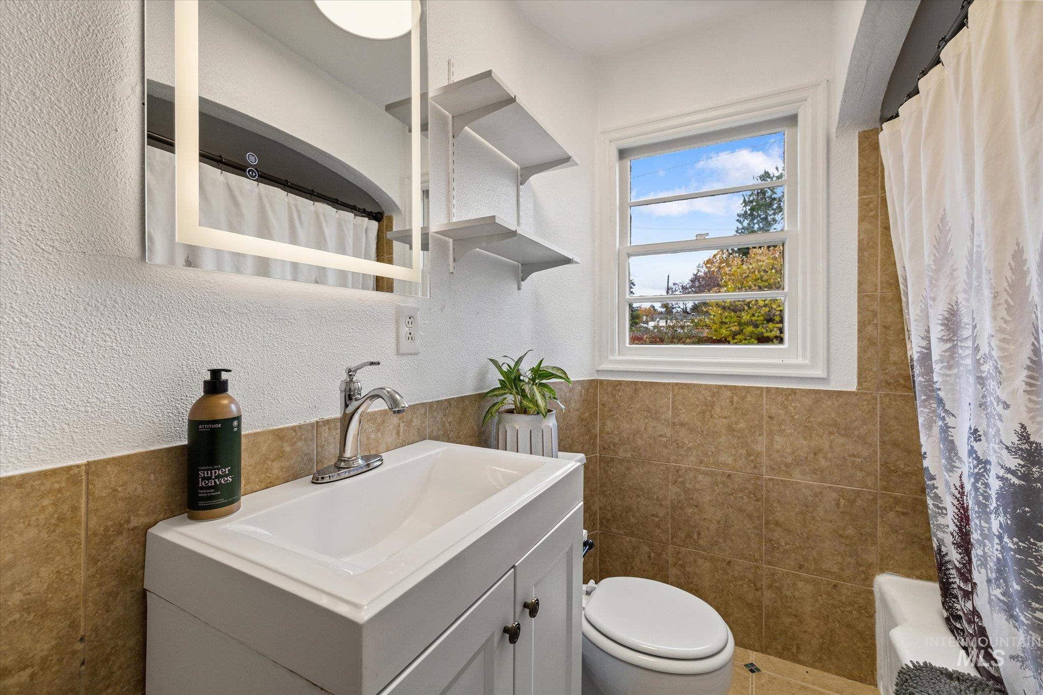 Bathroom with tile walls, vanity, a textured wall, and shower / bath combo