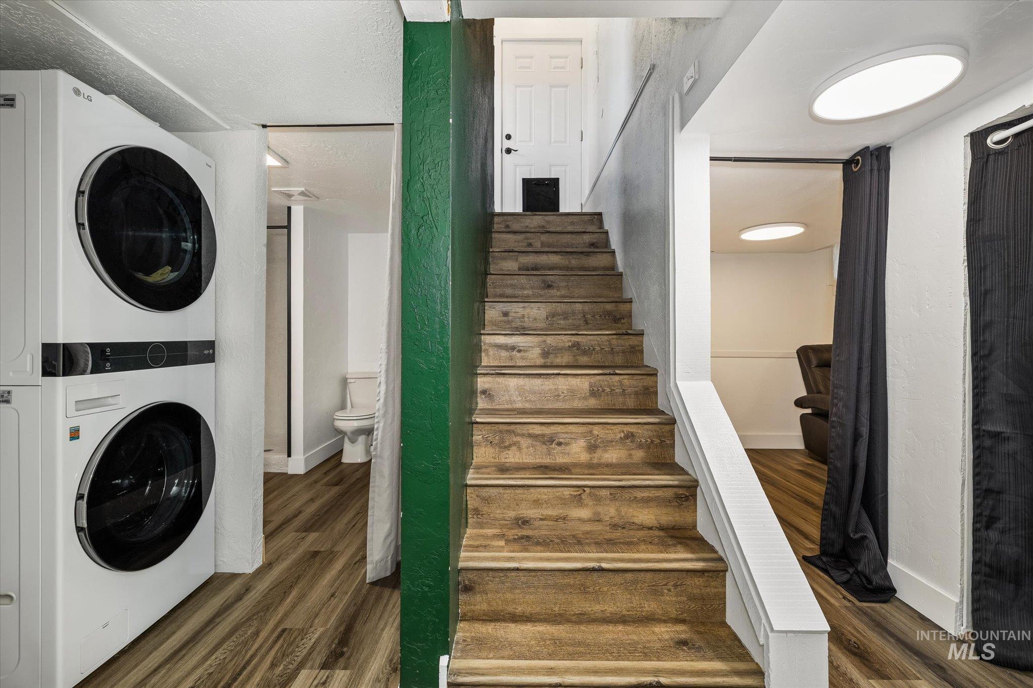 Staircase with wood finished floors, stacked washer / dryer, and a textured wall