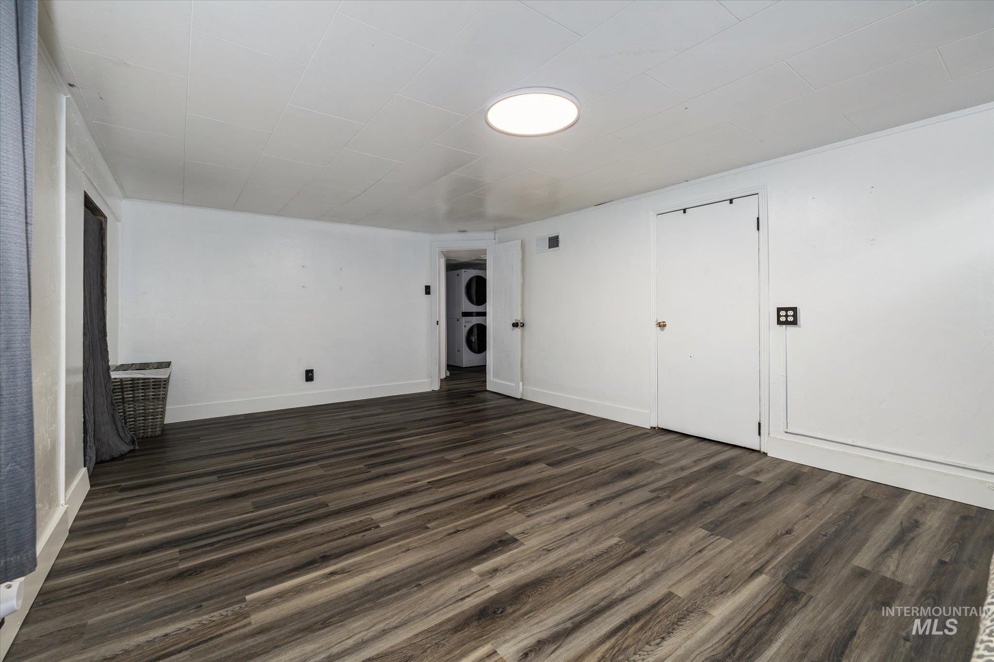 Unfurnished bedroom with dark wood-type flooring and stacked washer and clothes dryer