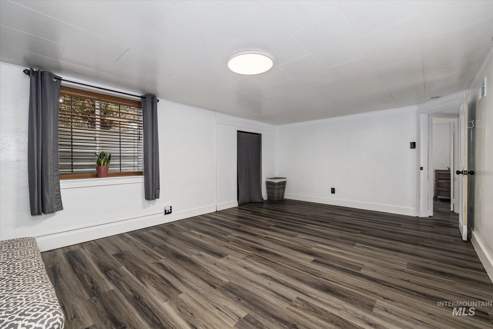 Unfurnished living room featuring dark wood-style flooring and baseboards
