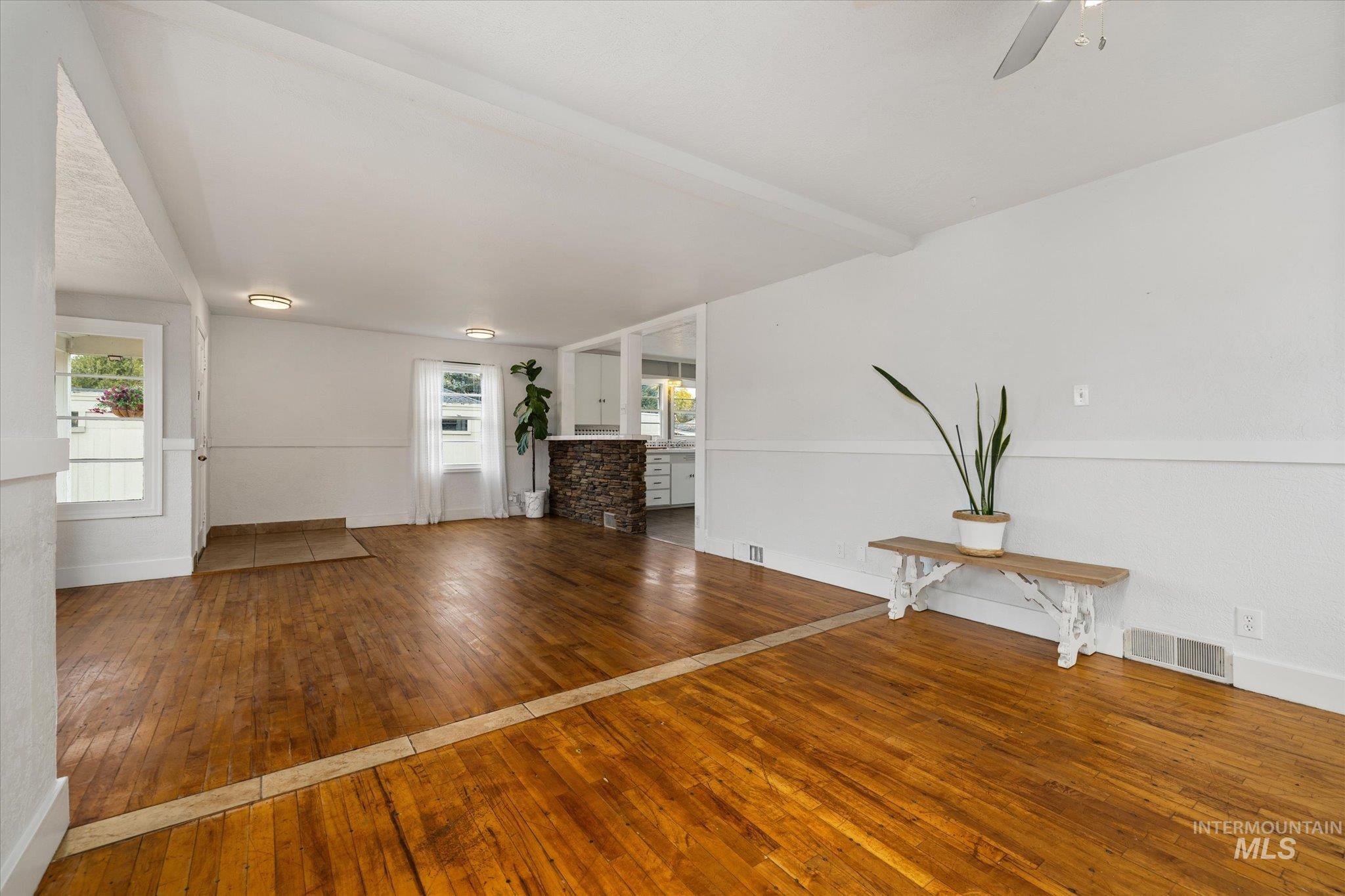 Unfurnished living room featuring hardwood / wood-style flooring, beam ceiling, and a ceiling fan