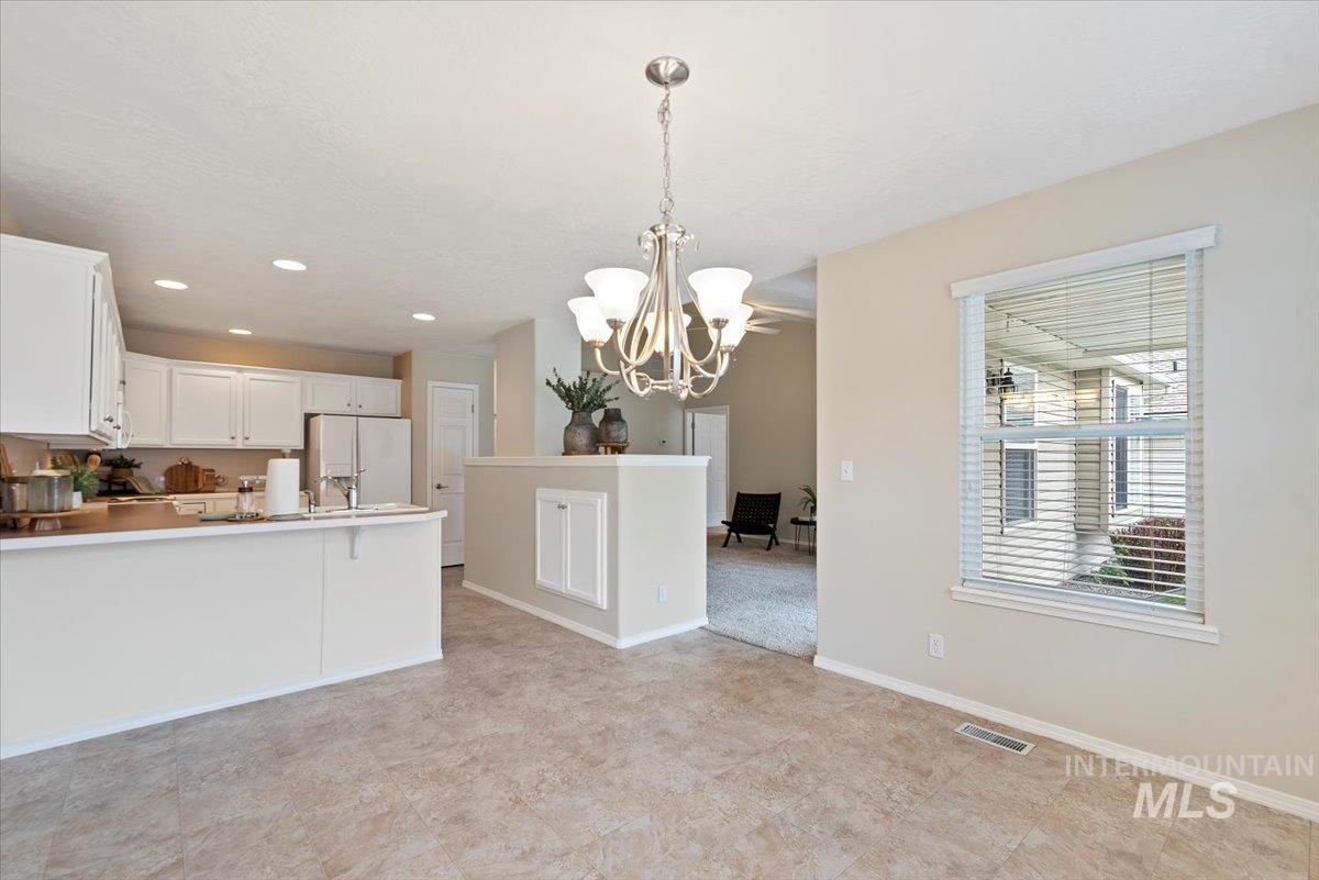 Kitchen featuring white cabinets, white refrigerator with ice dispenser, a peninsula, light countertops, and decorative light fixtures