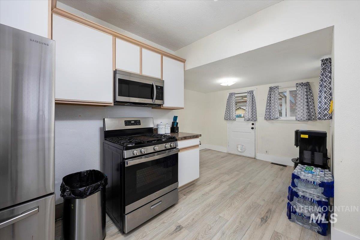 Kitchen featuring stainless steel appliances, light wood style floors, white cabinets, and dark countertops