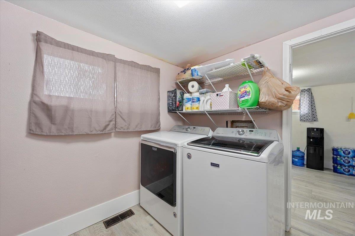 Laundry room featuring light wood-style floors, a textured ceiling, and washer and clothes dryer