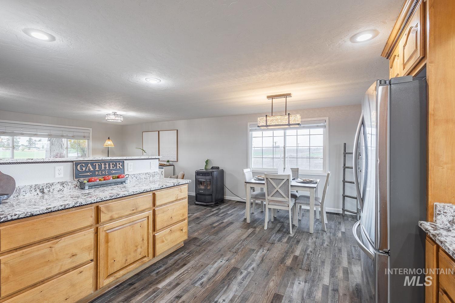 Kitchen with light stone counters, freestanding refrigerator, dark wood-style flooring, light brown cabinetry, and hanging light fixtures