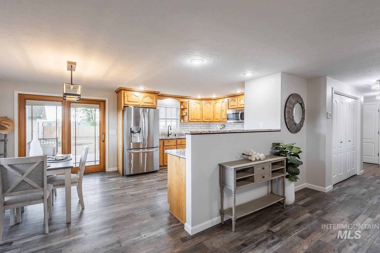 Kitchen featuring stainless steel appliances, hanging light fixtures, tasteful backsplash, light stone countertops, and dark wood finished floors