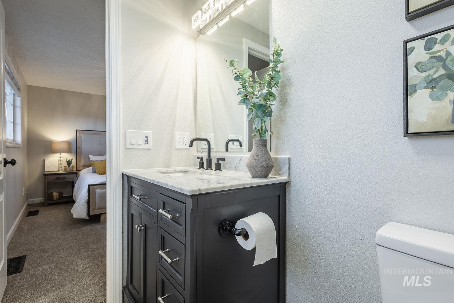 Ensuite bathroom with vanity, a textured wall, and dark carpet