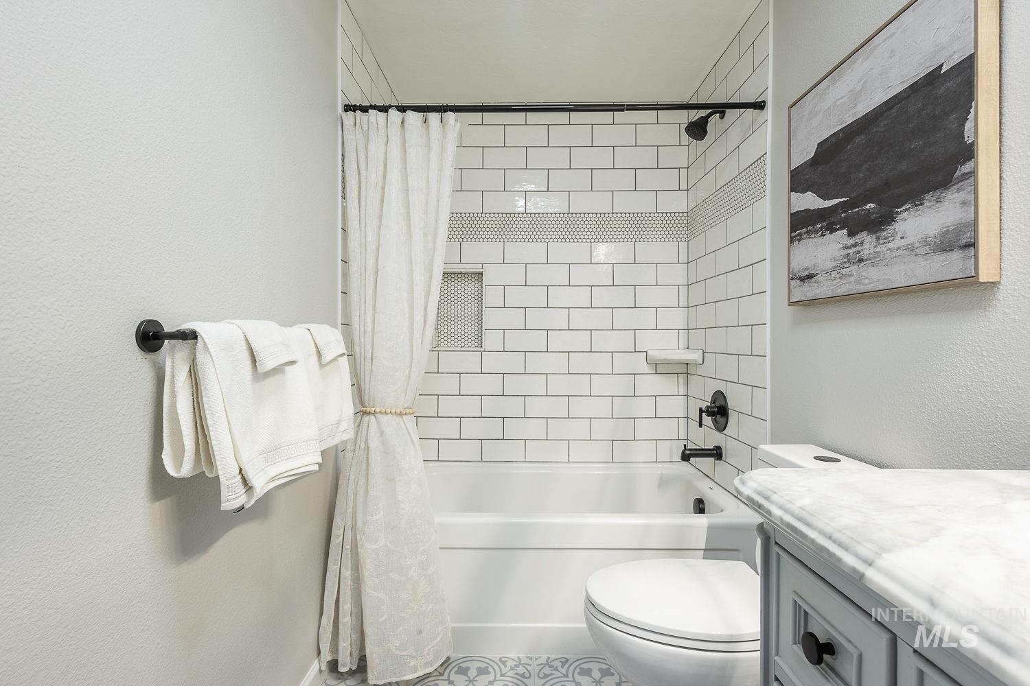 Bathroom with a textured wall, shower / bathtub combination with curtain, and vanity