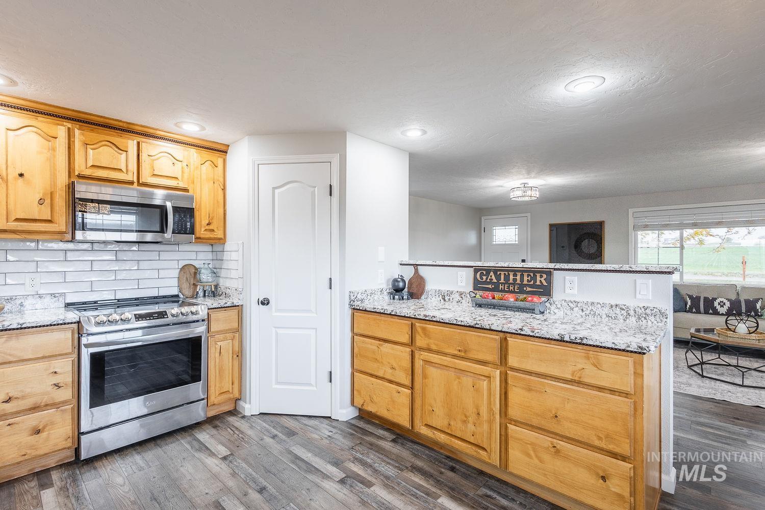 Kitchen with stainless steel appliances, light stone counters, decorative backsplash, dark wood-type flooring, and recessed lighting