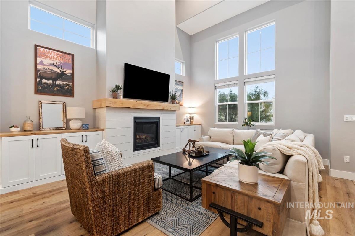 Living room featuring a high ceiling, healthy amount of natural light, a glass covered fireplace, and light wood-style floors