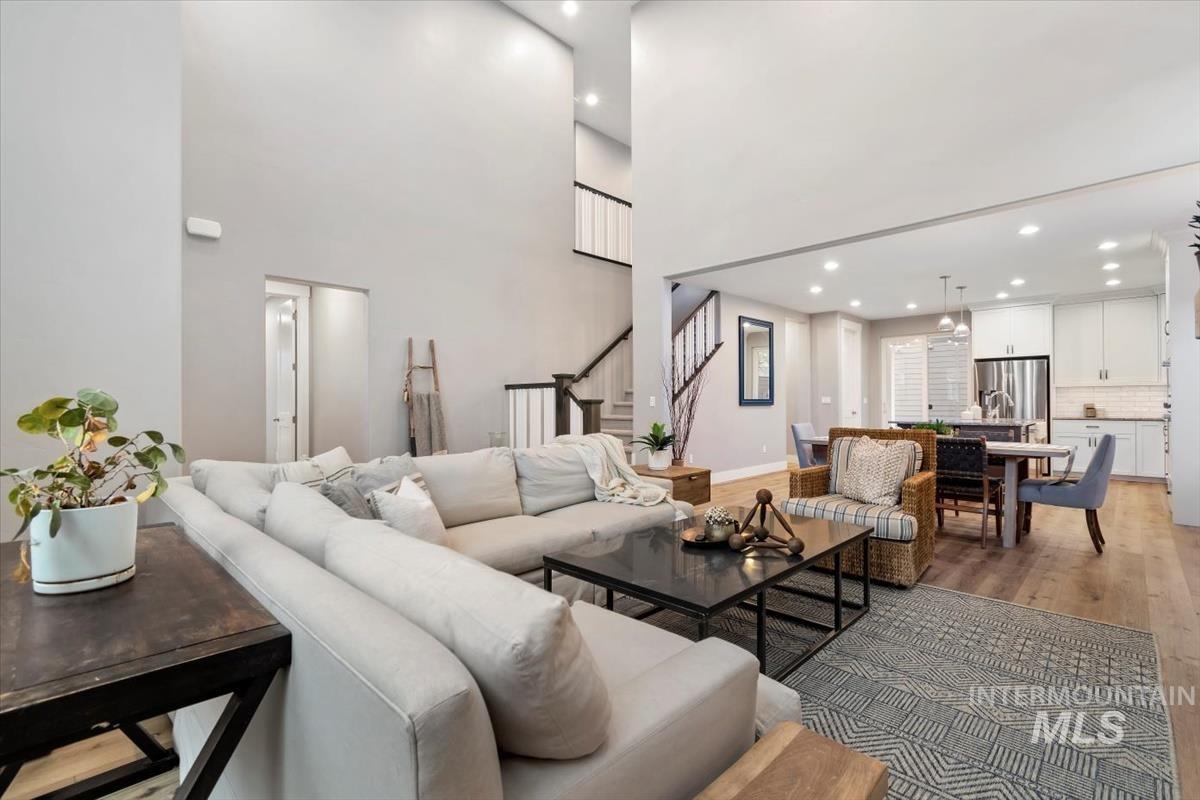 Living room with light wood finished floors, a high ceiling, recessed lighting, and stairway