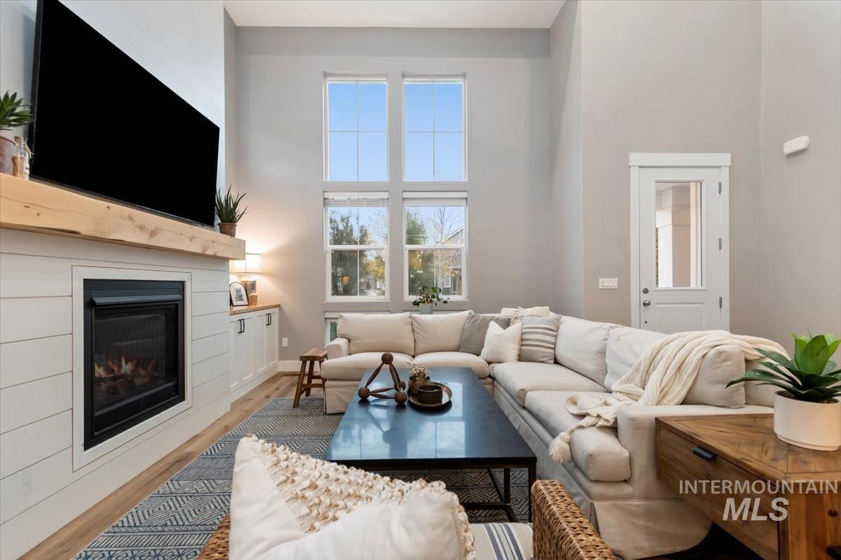 Living area featuring wood finished floors, a towering ceiling, and a glass covered fireplace