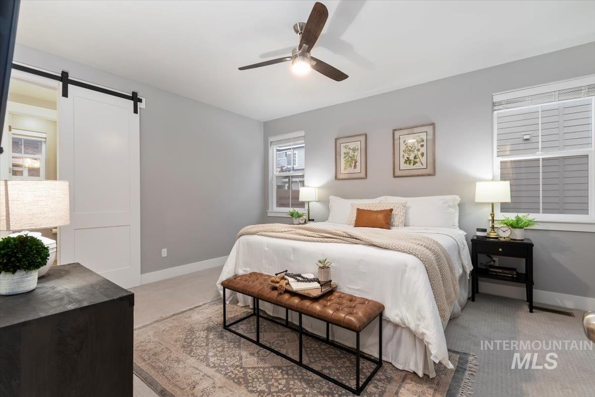 Bedroom featuring light colored carpet, a barn door, and a ceiling fan
