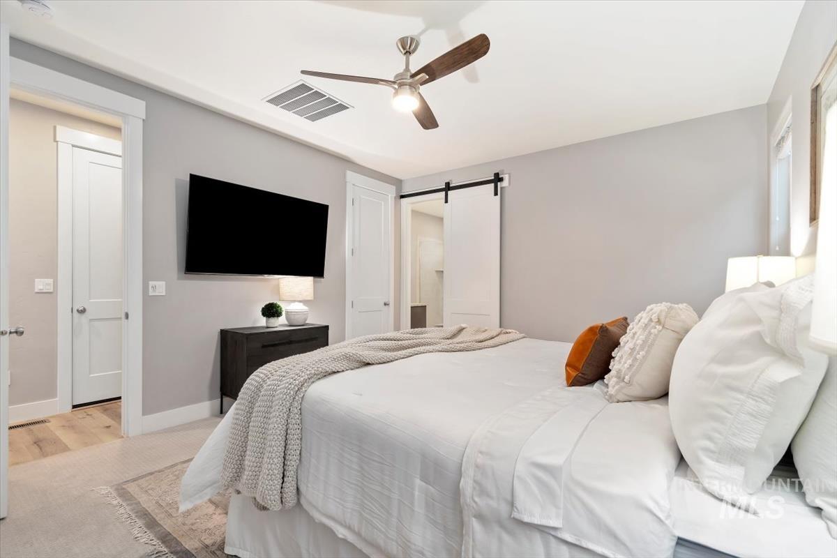 Bedroom with a barn door, a ceiling fan, and light carpet