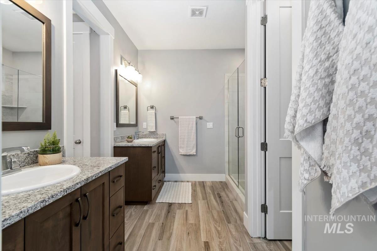 Full bathroom with a stall shower, two vanities, and light wood-style flooring