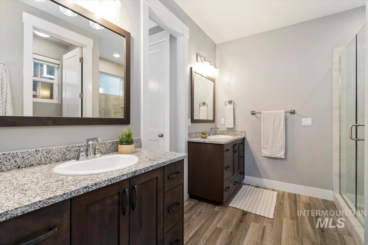 Full bath featuring light wood-type flooring, two vanities, and a shower stall