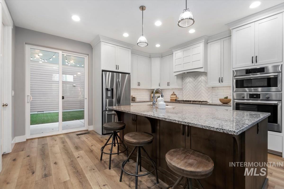 Kitchen featuring appliances with stainless steel finishes, light stone counters, decorative backsplash, white cabinets, and recessed lighting