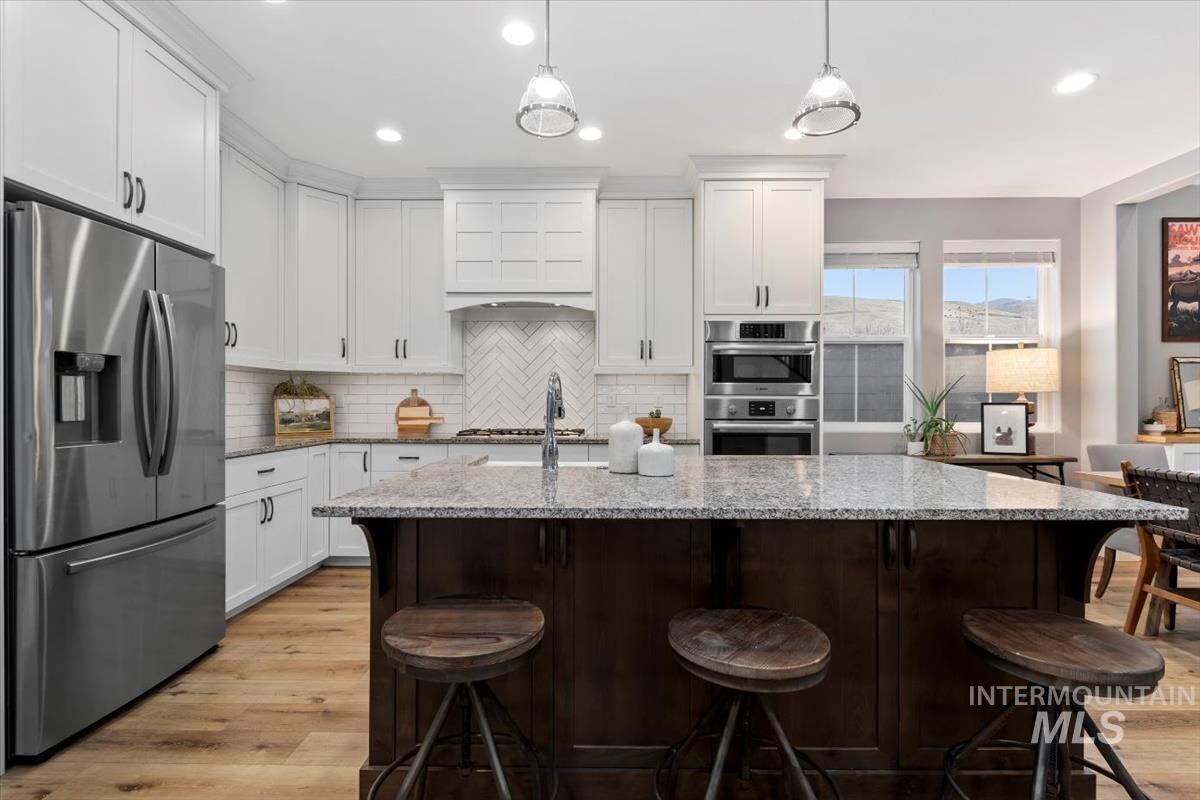Kitchen featuring appliances with stainless steel finishes, white cabinetry, light stone countertops, tasteful backsplash, and a breakfast bar