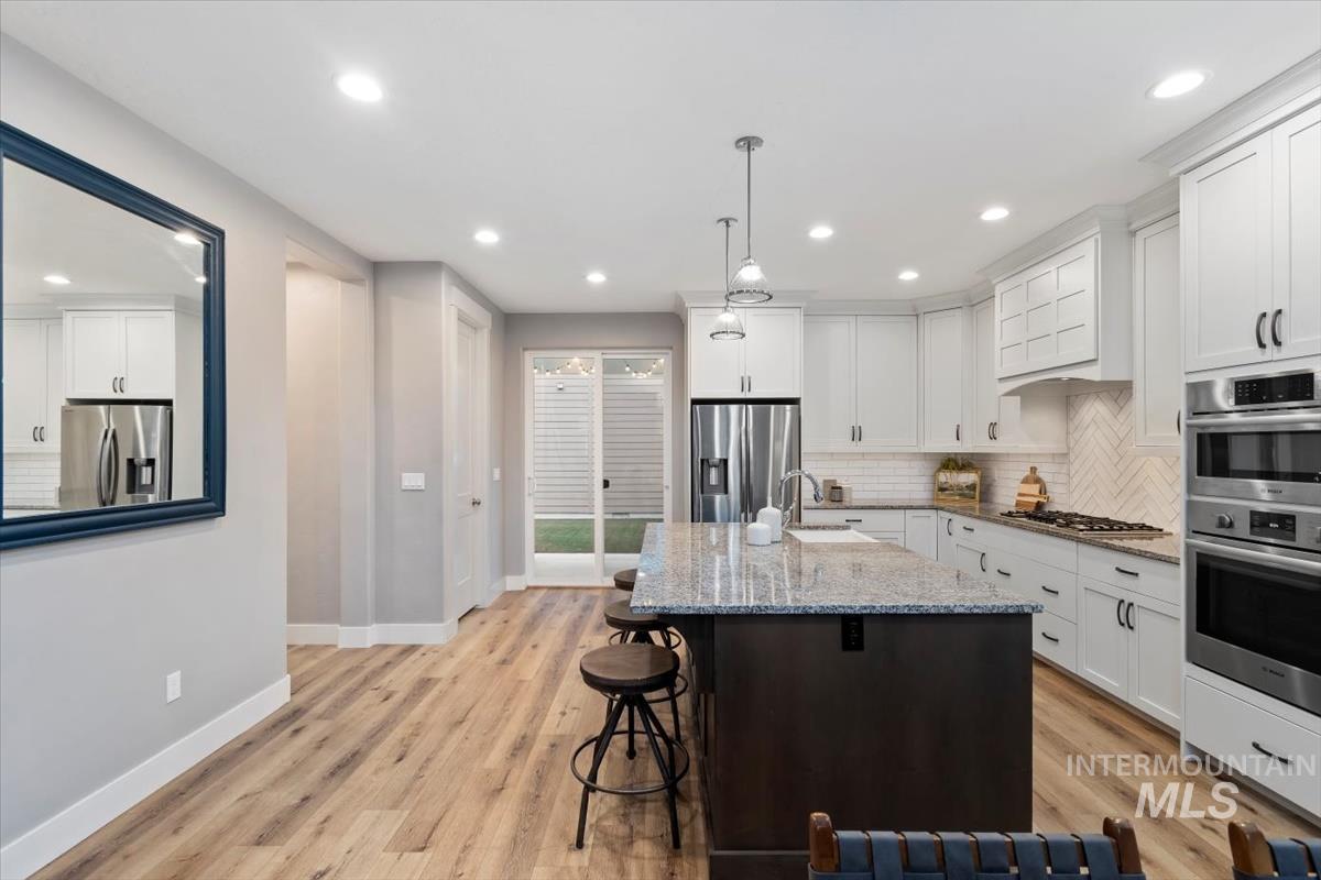 Kitchen featuring white cabinetry, light stone countertops, decorative backsplash, a kitchen breakfast bar, and a center island with sink