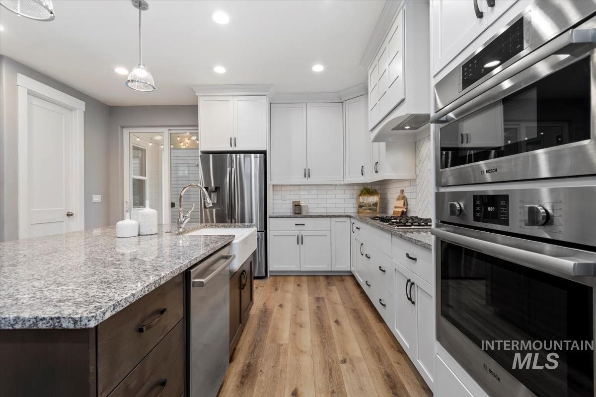 Kitchen with appliances with stainless steel finishes, decorative backsplash, white cabinetry, light wood finished floors, and recessed lighting