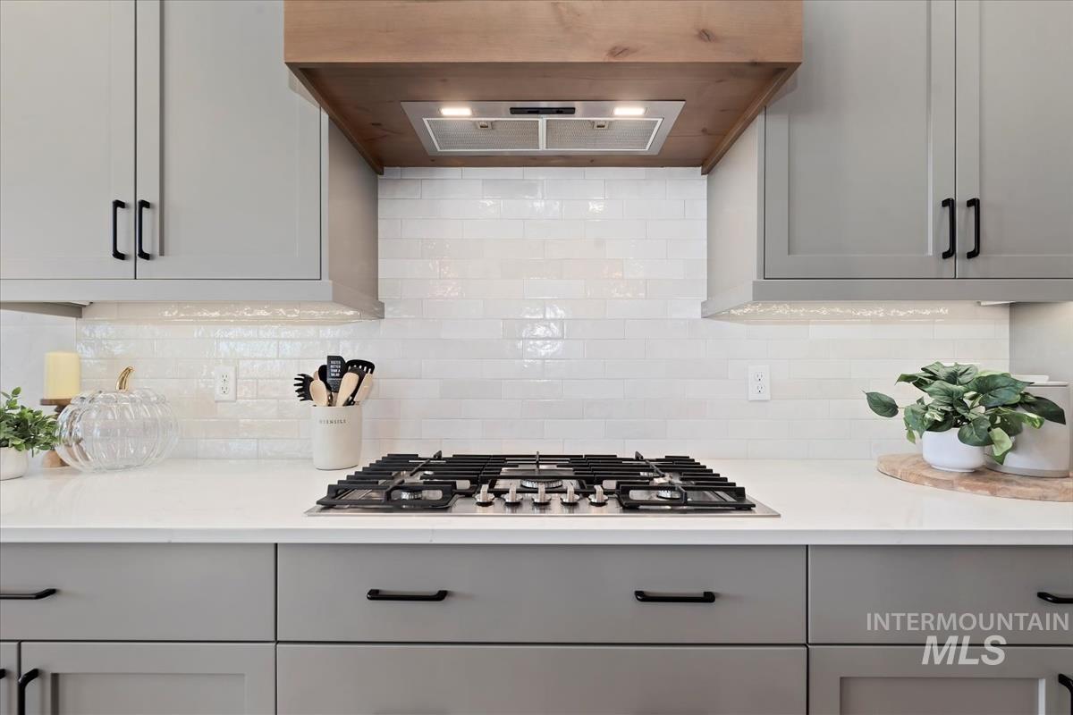 Kitchen featuring ventilation hood, backsplash, stainless steel gas cooktop, light stone counters, and gray cabinets
