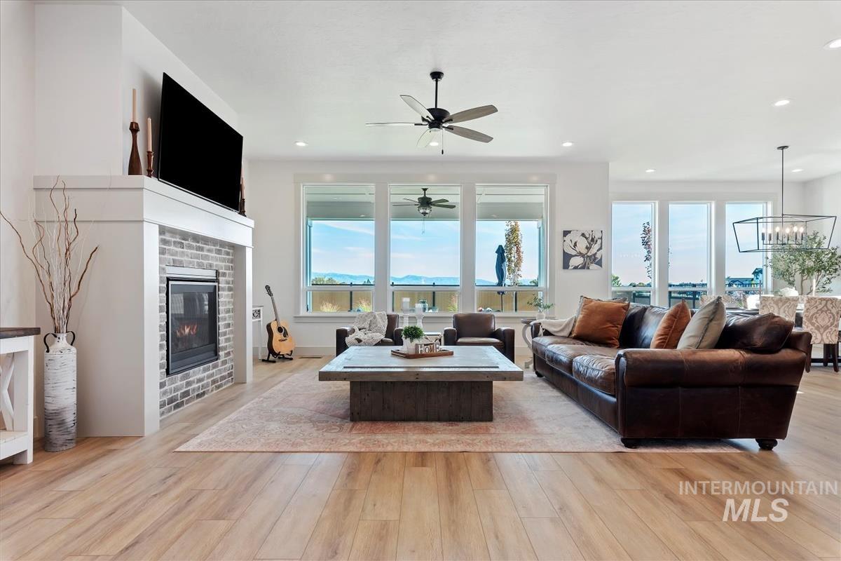 Living area with light wood-style flooring, healthy amount of natural light, a brick fireplace, a ceiling fan, and recessed lighting