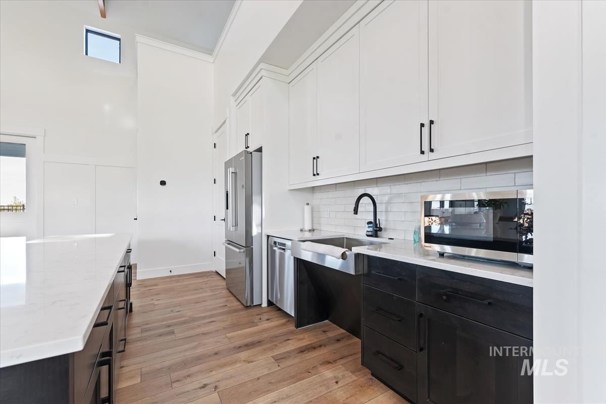 Kitchen featuring white cabinetry, light wood finished floors, light stone counters, stainless steel appliances, and backsplash
