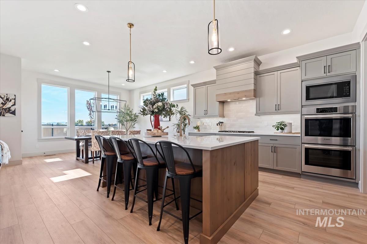 Kitchen featuring decorative light fixtures, tasteful backsplash, gray cabinets, stainless steel appliances, and a center island with sink
