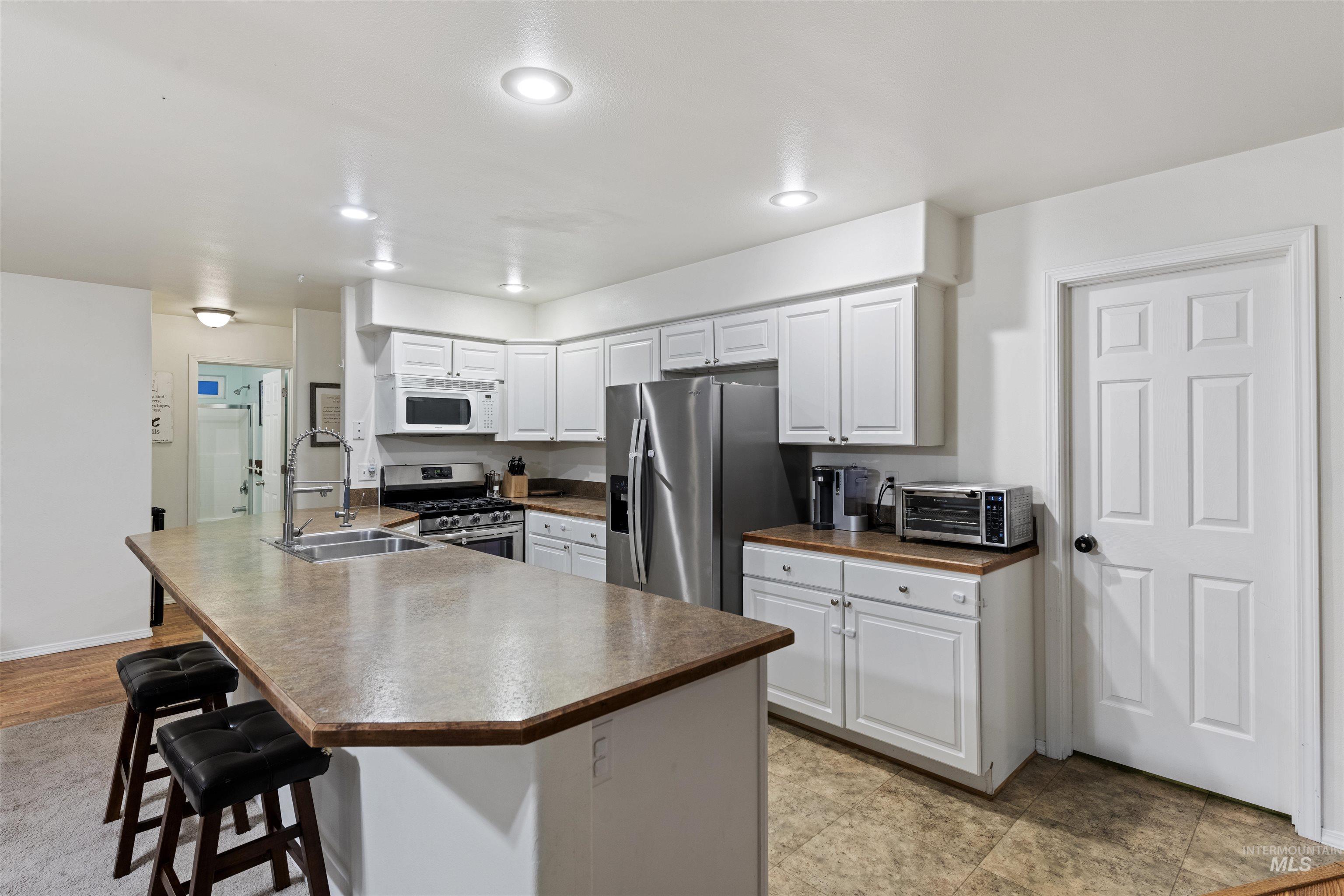 Kitchen featuring stainless steel appliances, a breakfast bar area, dark countertops, white cabinetry, and recessed lighting