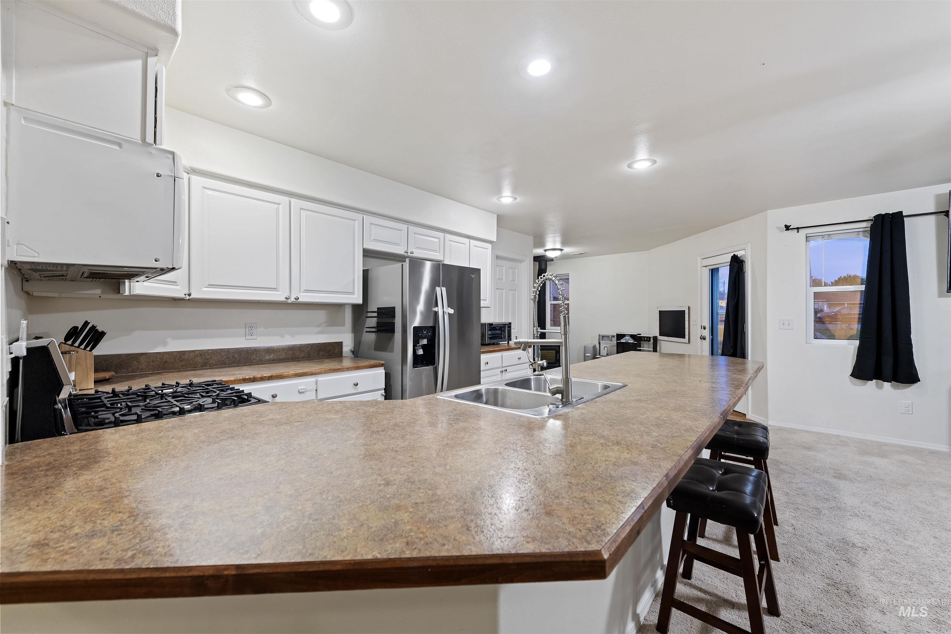 Kitchen featuring a peninsula, white cabinetry, stainless steel fridge, a breakfast bar area, and black gas range