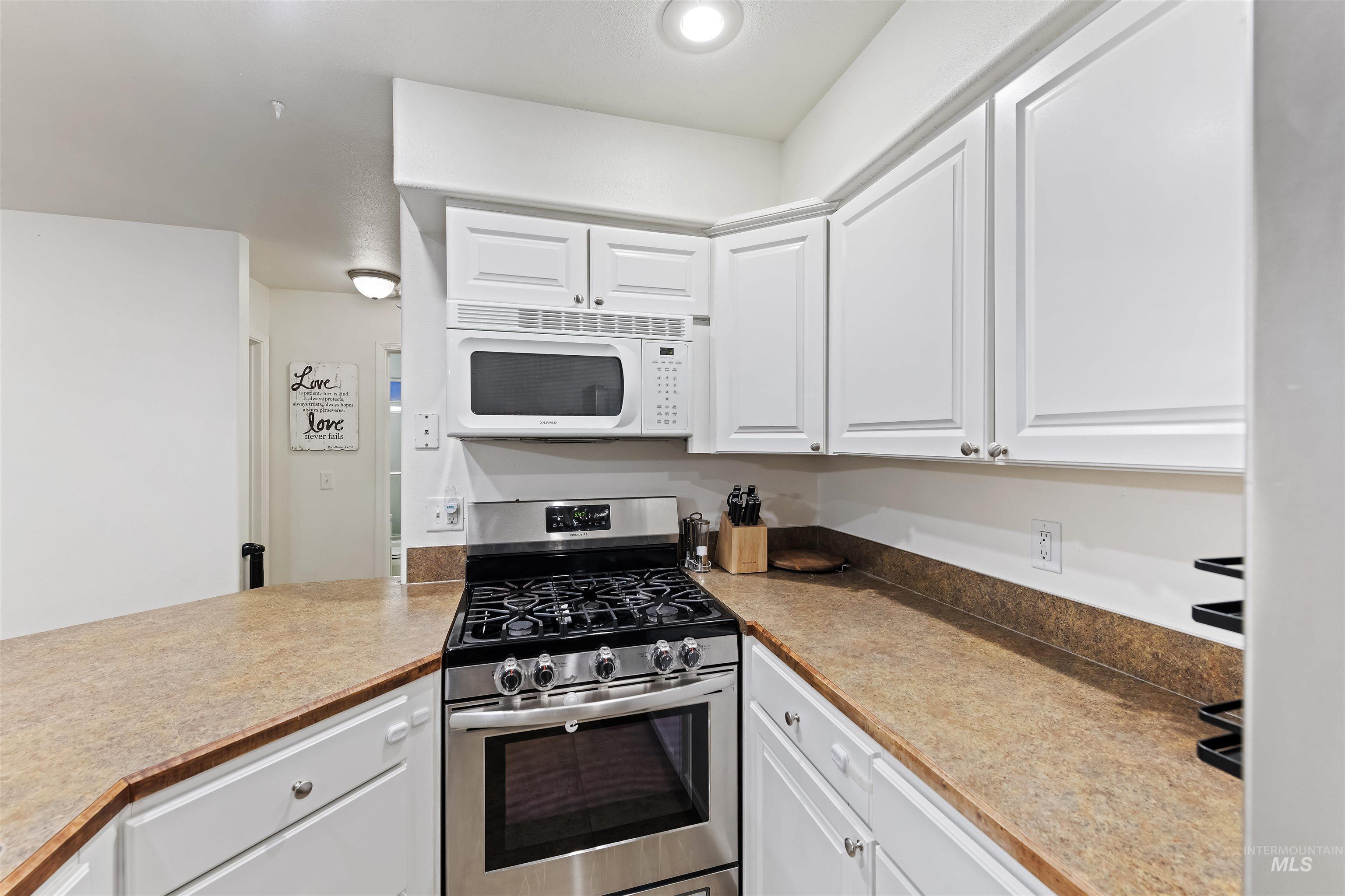 Kitchen with gas stove, white cabinetry, and white microwave