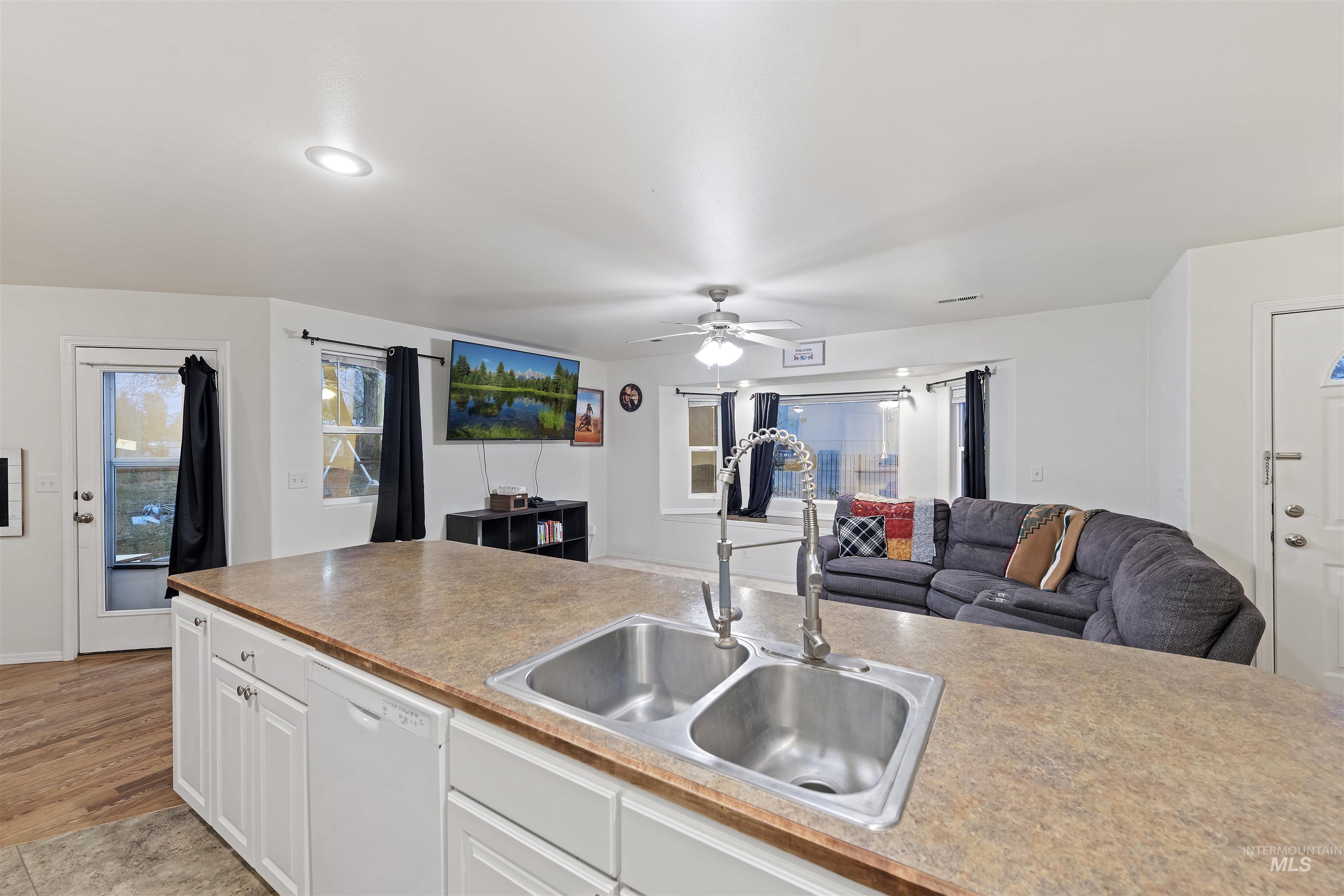 Kitchen featuring white cabinetry, open floor plan, dishwasher, and ceiling fan